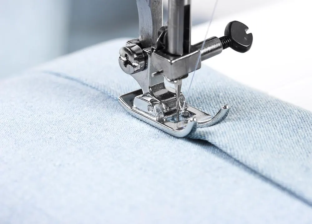 Pied de biche d’une machine à coudre piquant un tissu bleu clair